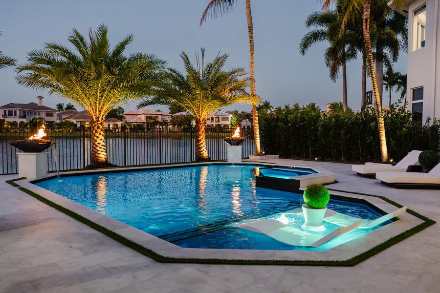 Backyard pool and spa at dusk flanked by lit fire bowls